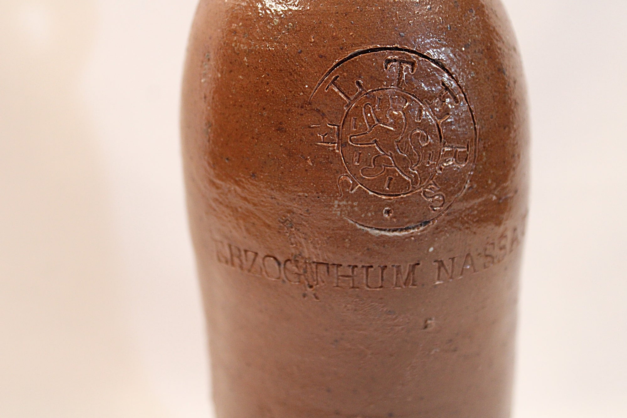 Antique ceramic bottle with embossed design and text on a white background