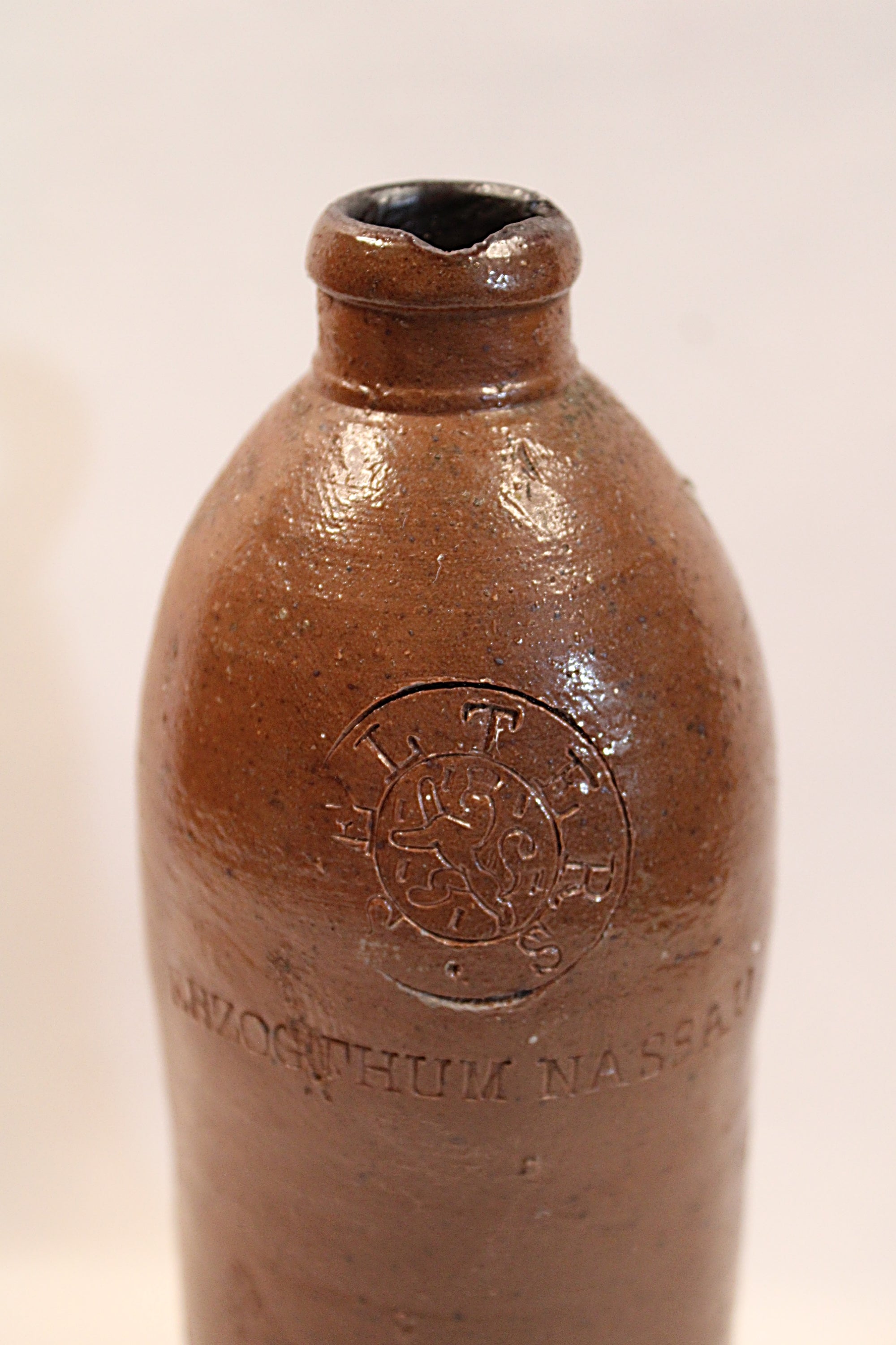 Antique  Brown ceramic bottle with embossed design on a beige back ground