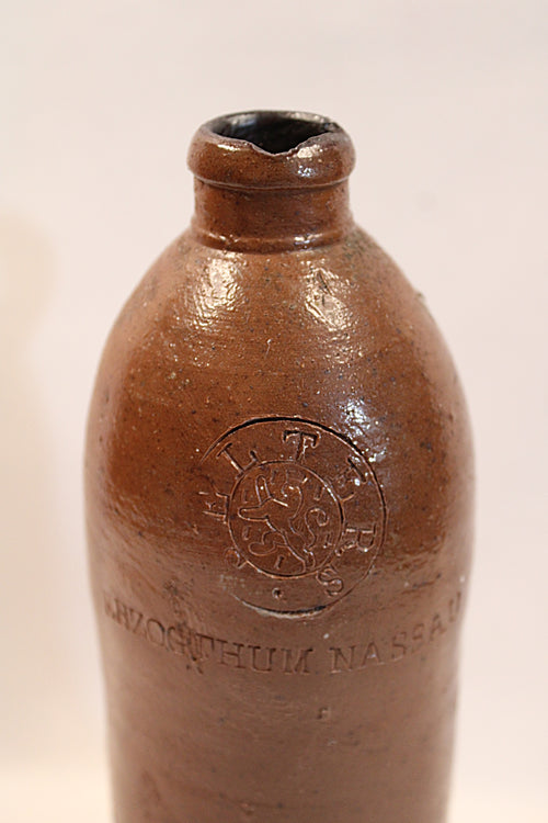Antique  Brown ceramic bottle with embossed design on a beige back ground