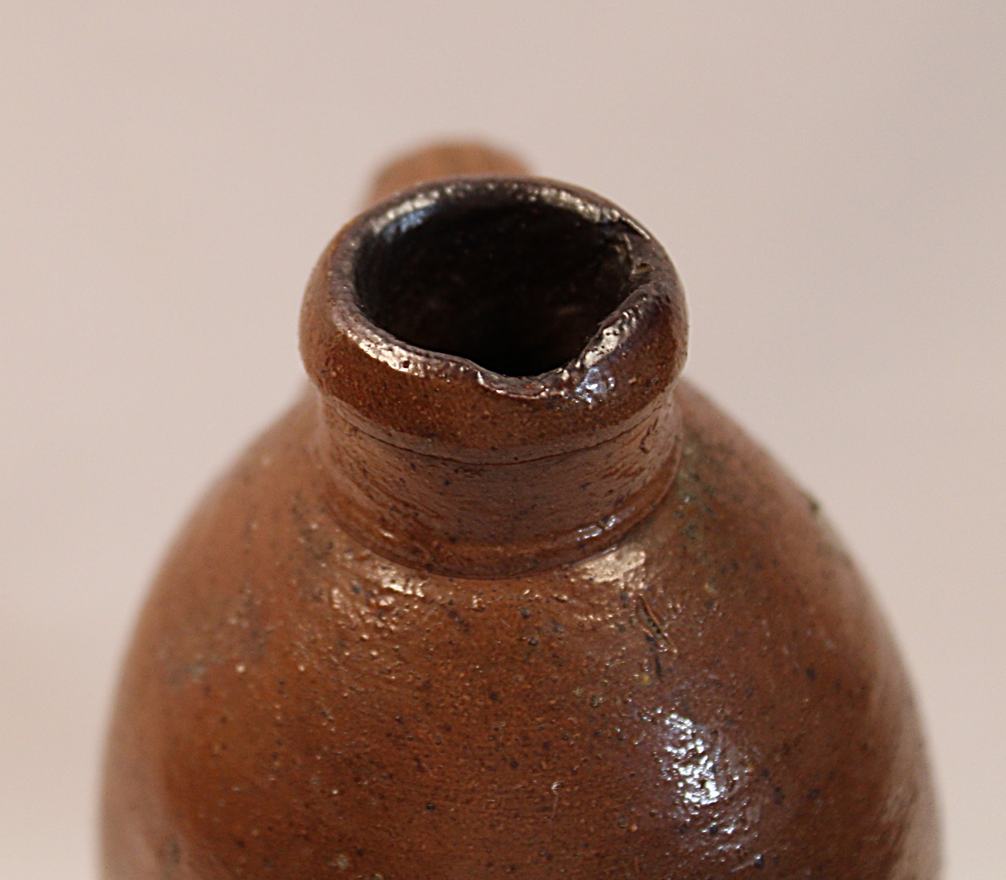 Close-up of a brown ceramic bottle neck on a beige background handle back