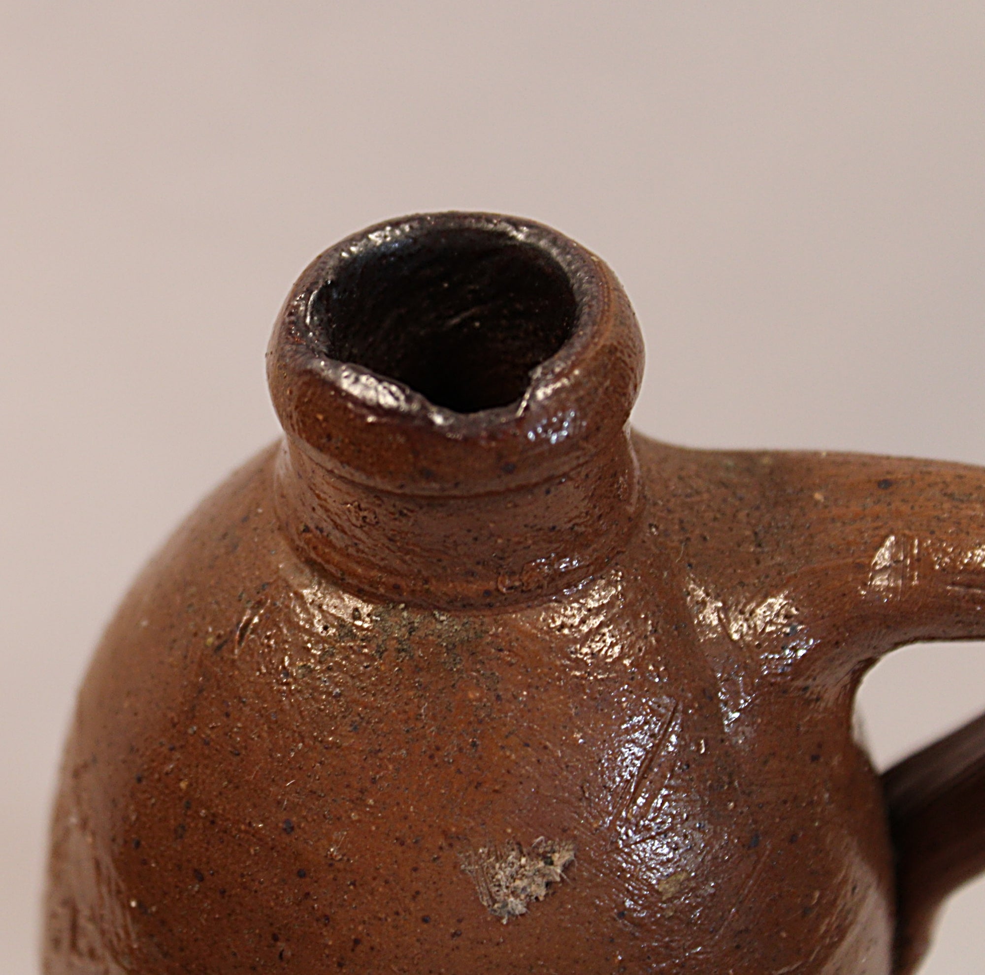 Close-up of antique brown ceramic bottle with a handle on a beige background