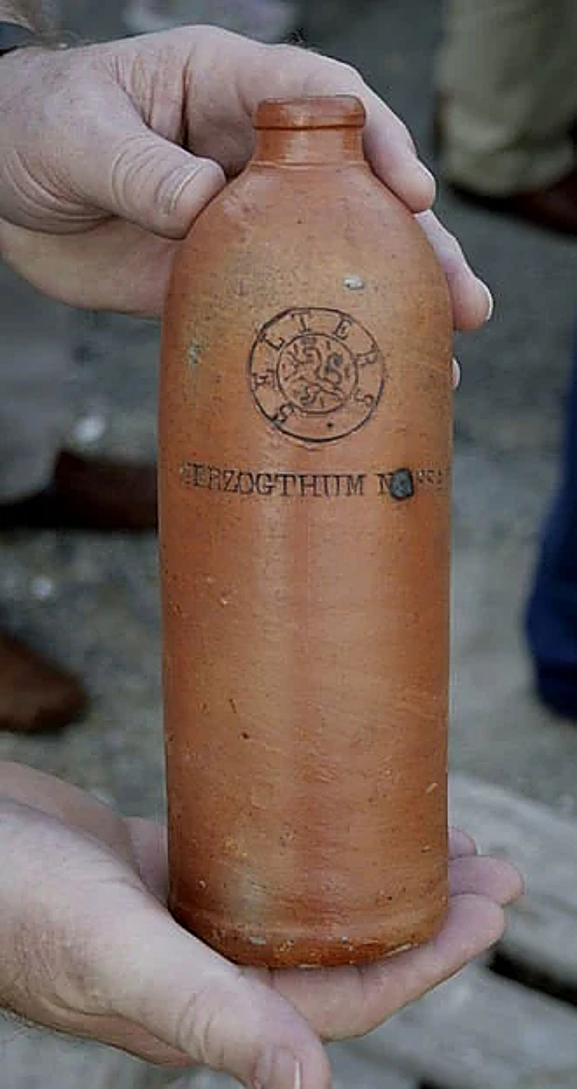 Person holding a antique terracotta bottle with visible branding against a blurred background