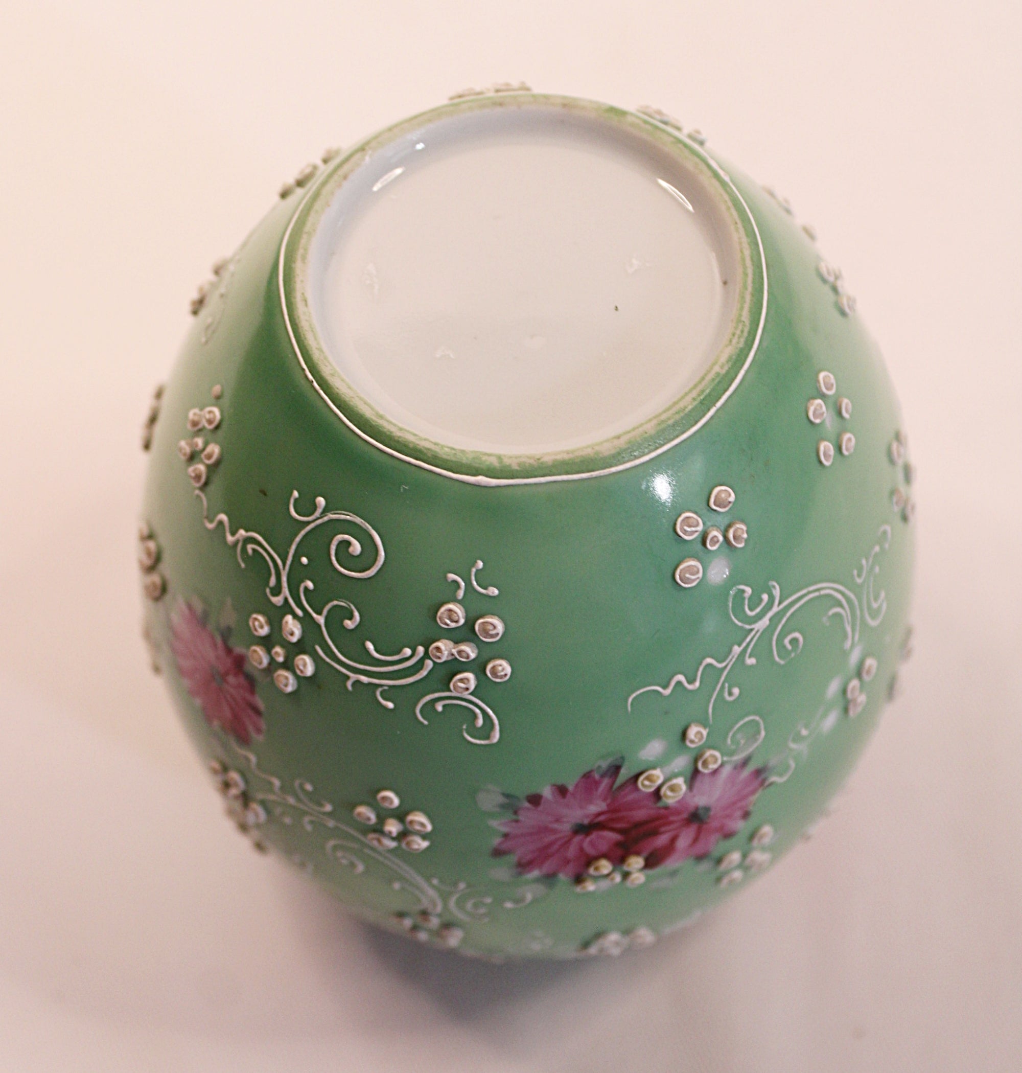 Decorative green vase with floral patterns on a light background showing bottom