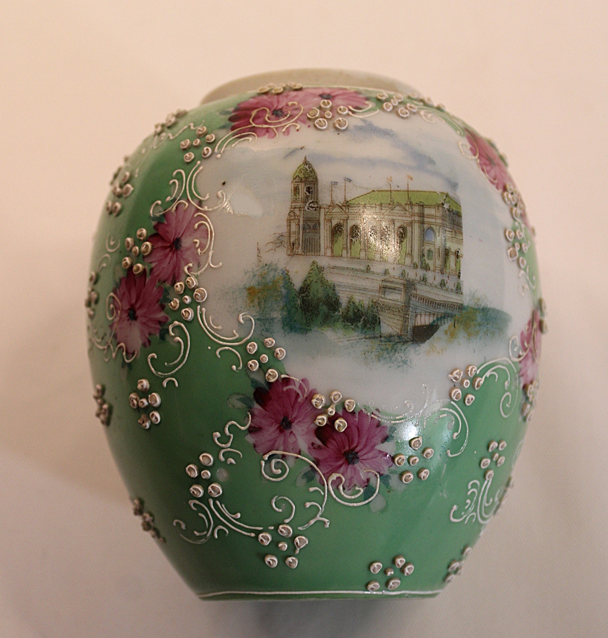 Decorative ceramic vase with floral patterns and architectural scene on a light pink and green background