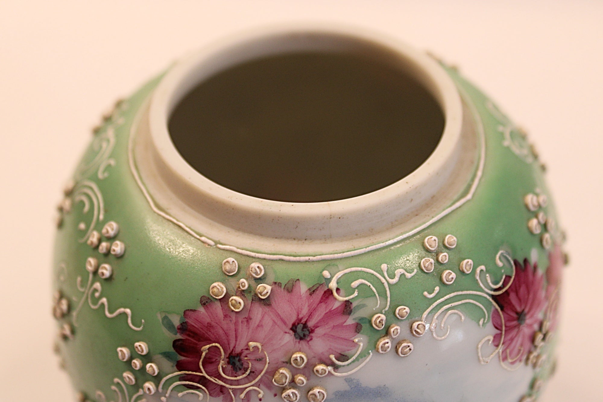 Decorative ceramic jar with floral patterns on a beige background showing rim