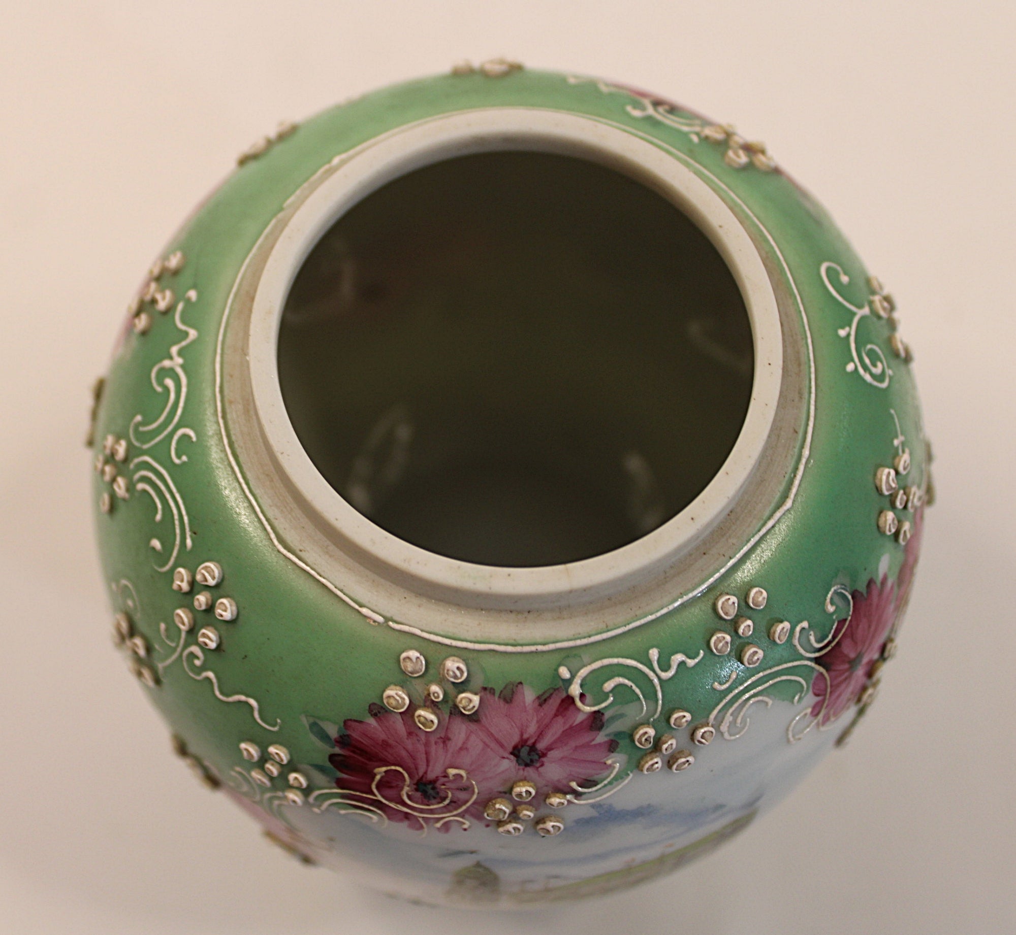 Decorative ceramic jar with floral patterns on a plain background showing rim opening