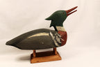 Wooden duck decoy on a stand against a plain background