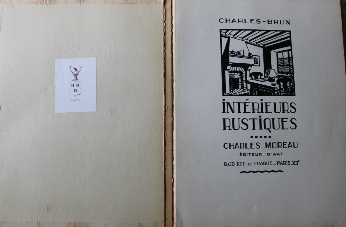 Open vintage book showing the left page with a small white label and the right page with black printed cover text reading 'CHARLES-BRUN' and 'INTERIEURS RUSTIQUES' by Charles-Moiseau.