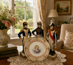 Decorative display of figurines and a plate in a room with a window and lamp.