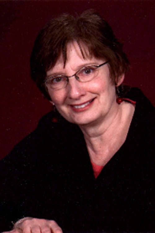 Diane Ulmer Pedersen  wearing glasses and a black sweater against a red background