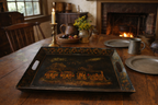 Vintage wooden table with a decorative tray, candles, and a fireplace in the background.