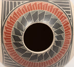 Close-up of a hand-painted ceramic pot featuring a circular geometric pattern with black, terracotta red, and beige hand-painted designs.
