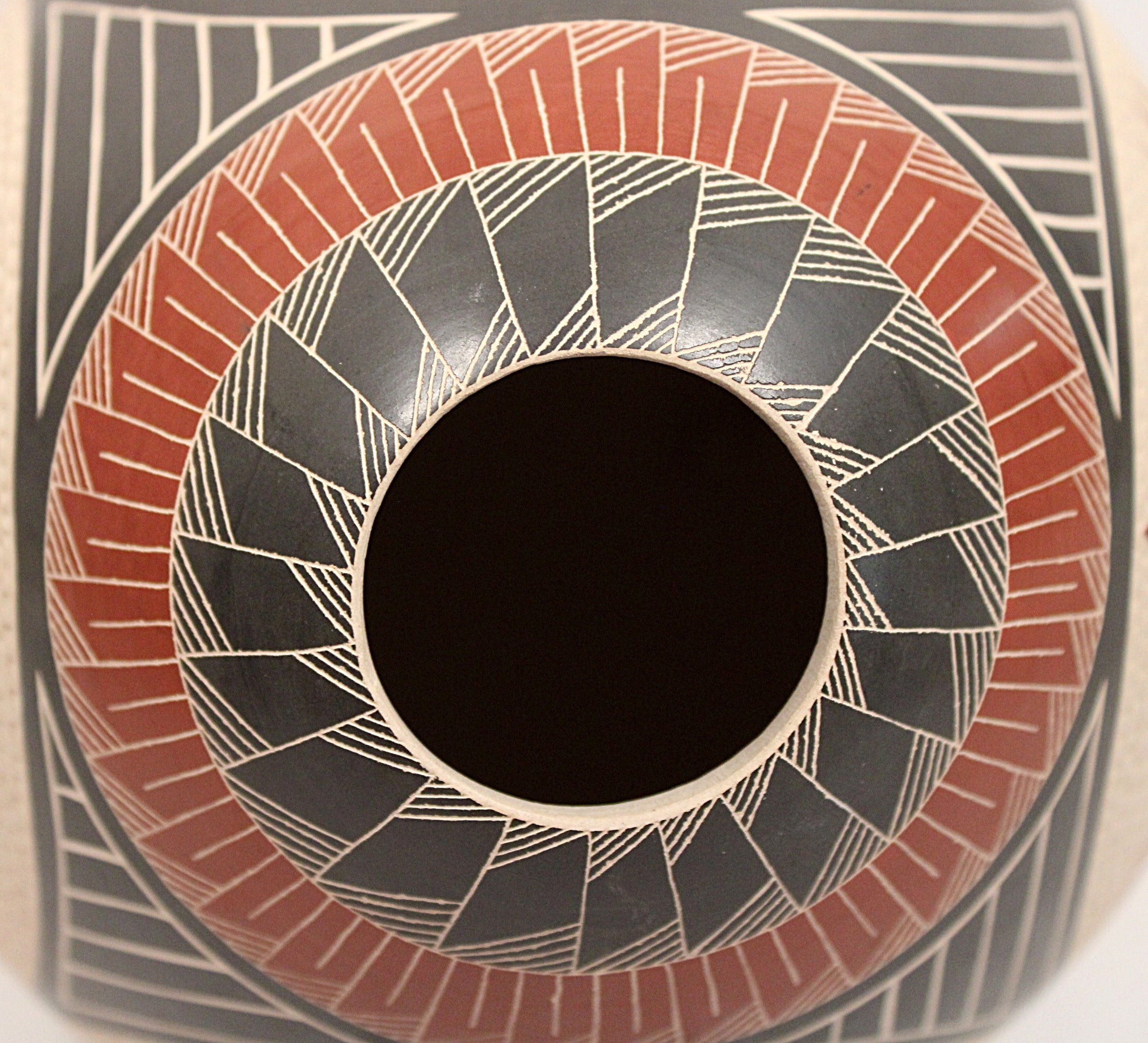 Close-up of a hand-painted ceramic pot featuring a circular geometric pattern with black, terracotta red, and beige hand-painted designs.