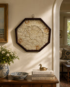 Decorative Sailors Valentine wall piece on a wall with a wooden side table below containing books, a vase, and a small sculpture.