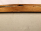 Close-up of a wooden frame or board with a small metal latch near the top center, set against a light beige fabric background.