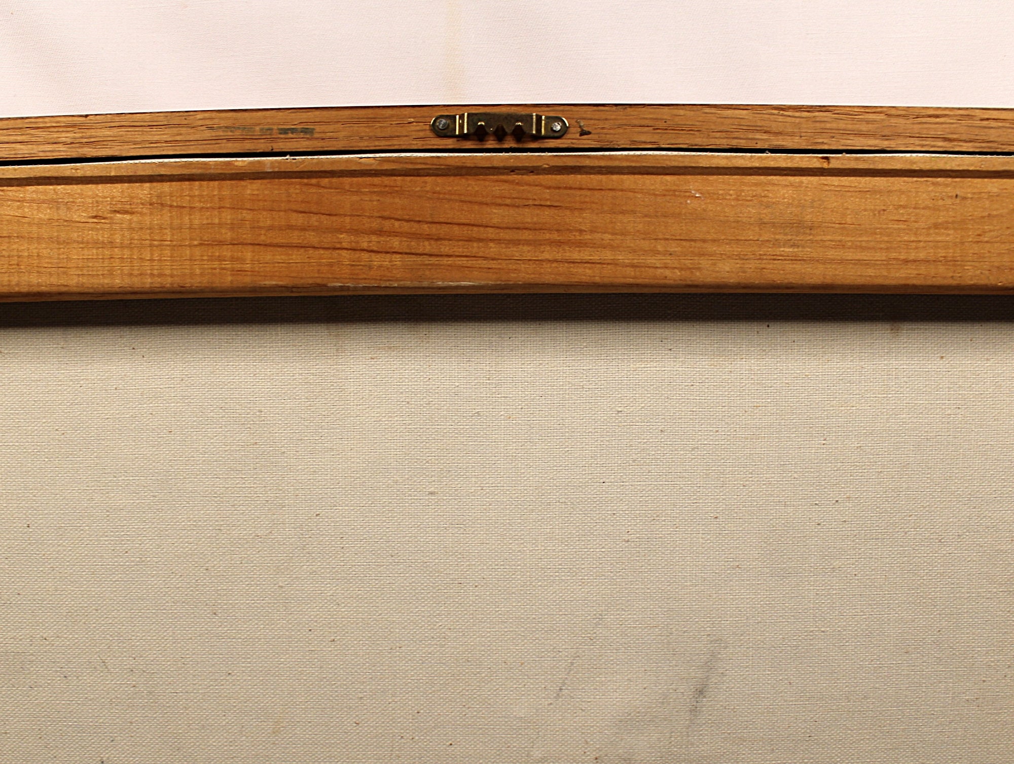 Close-up of a wooden frame or board with a small metal latch near the top center, set against a light beige fabric background.