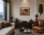 A framed Native American painting of ceramic bowls hangs on a beige wall in a styled living room with a leather armchair, patterned pillows, a wooden console, and a window view. by Yellowhair