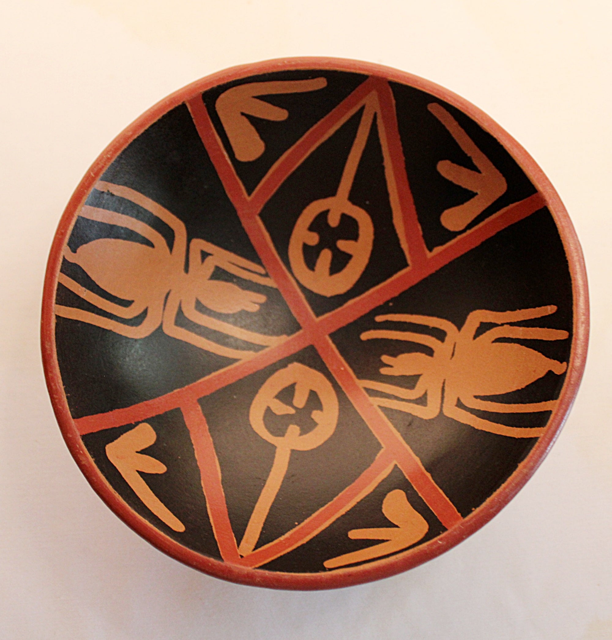 A round hand-painted ceramic bowl with a black interior decorated with terracotta-colored geometric lines and spider motifs, photographed from directly above on a light background.