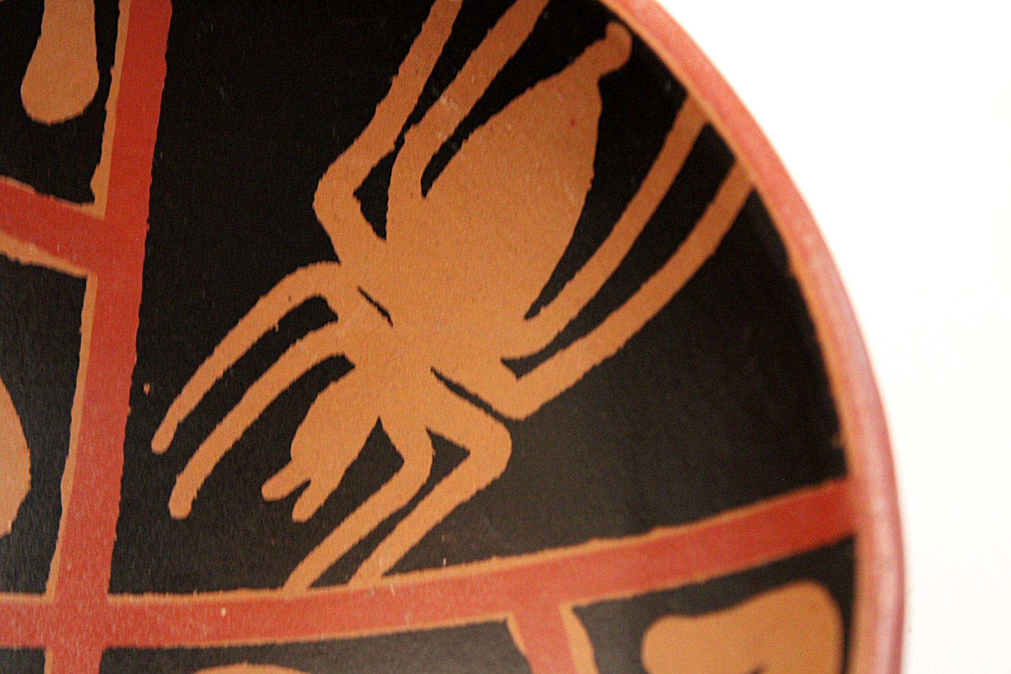 Close-up of a decorative ceramic plate or bowl featuring a stylized spider motif in terracotta orange on a black background, with a red-orange rim visible against a white backdrop.