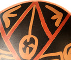 Close-up of a black ceramic surface decorated with orange geometric lines and stylized symbols.