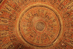 A close-up of a circular woven basket with concentric rings in natural tan, brown, orange, and red tones, filling the entire frame.