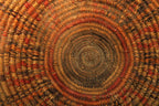 Close-up of a hand-woven circular basket with concentric rings in natural tan, brown, and rust red tones.