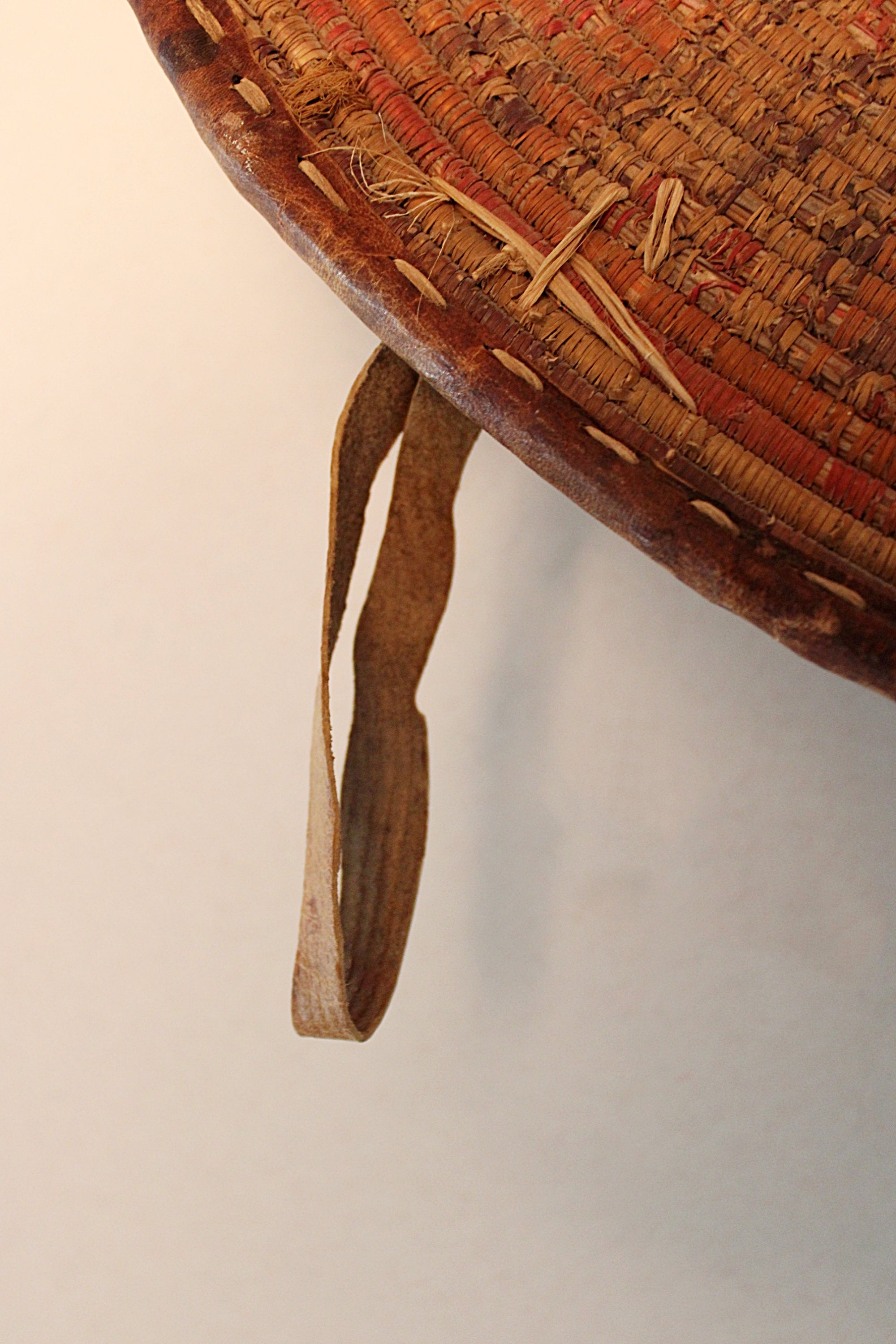 Close-up of a woven basket with a brown leather strap hanging down, photographed against a plain light background.