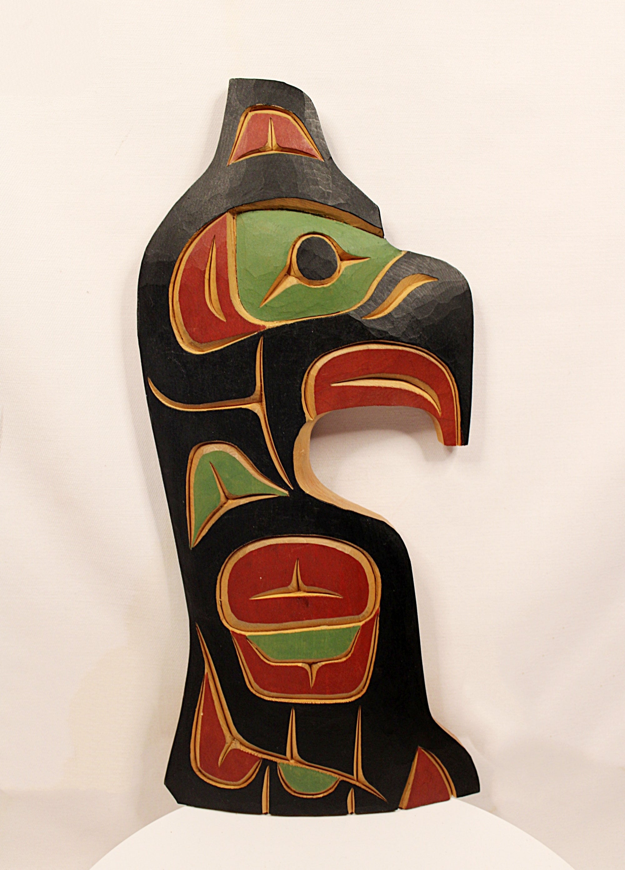 A hand-carved wooden totem pole sculpture featuring traditional Indigenous Pacific Northwest design elements in black, red, green, and gold, displayed against a plain white background.