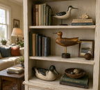Bookshelf with decorative birds, books, and a framed picture in a home setting. the bird in the middle is signed Seth 93