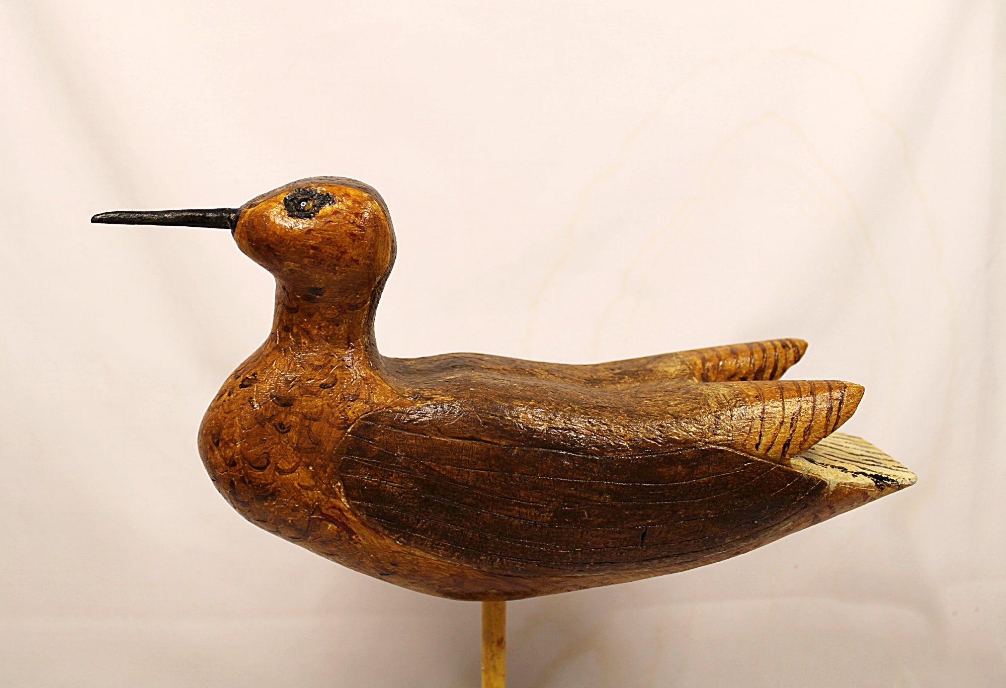 Wooden bird decoy on a stand against a plain background Facing left