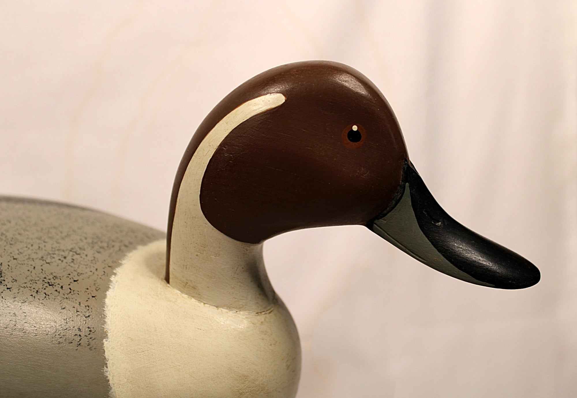 Wooden duck decoy with brown head and black bill on a plain background Facing Right