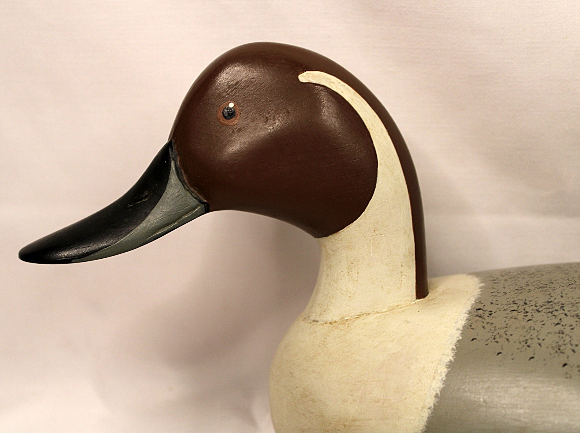 Close-up of a duck decoy with a brown head and black beak on a beige background Facing left