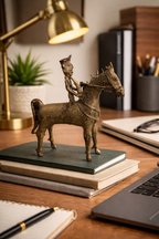 Bronze figurine of a horse and rider on a desk with a lamp, books, and laptop.